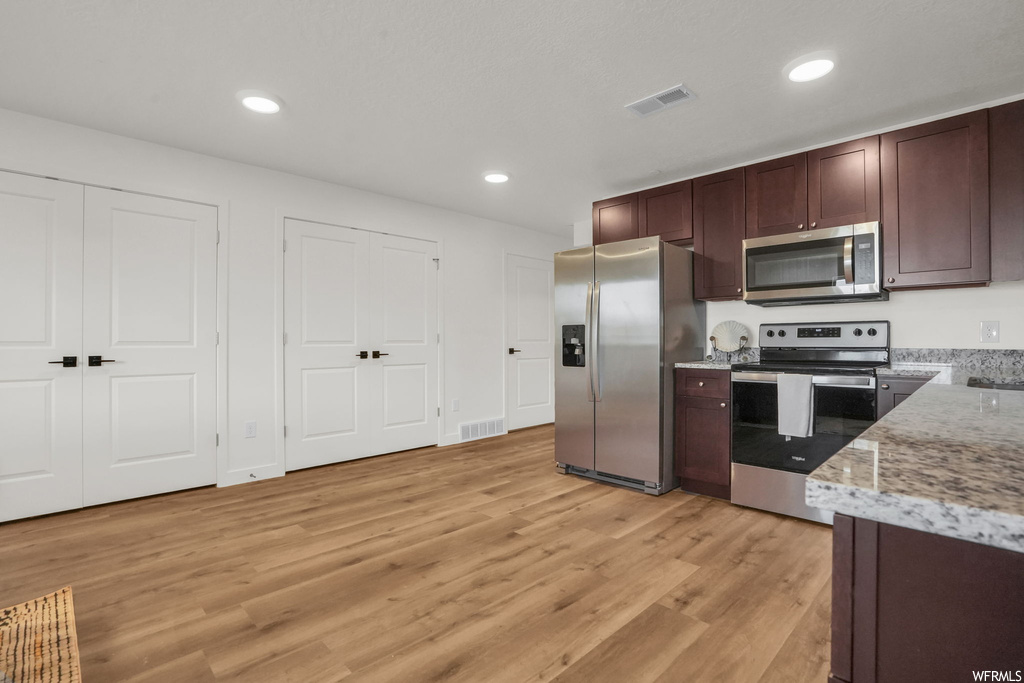 Kitchen with light hardwood / wood-style flooring, light stone counters, and appliances with stainless steel finishes