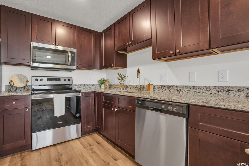 Kitchen with sink, light stone counters, light hardwood / wood-style flooring, appliances with stainless steel finishes, and dark brown cabinetry