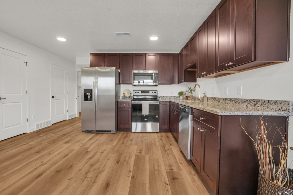 Kitchen featuring light hardwood / wood-style flooring, light stone countertops, sink, and stainless steel appliances