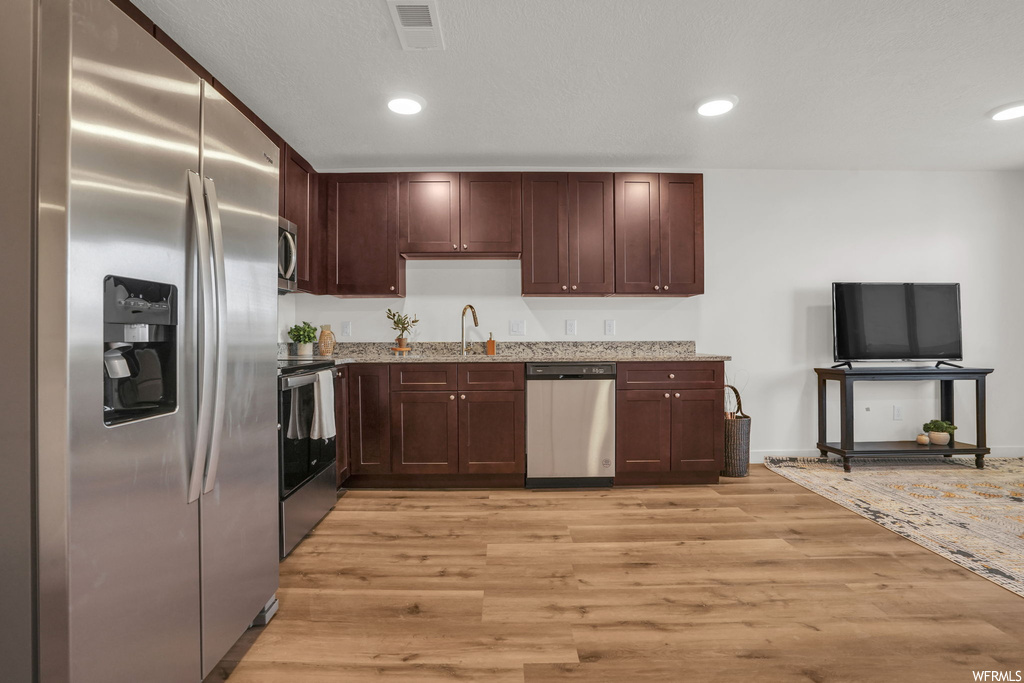 Kitchen with sink, appliances with stainless steel finishes, dark brown cabinets, light stone counters, and light wood-type flooring