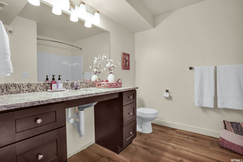 Bathroom with toilet, vanity with extensive cabinet space, and hardwood / wood-style flooring