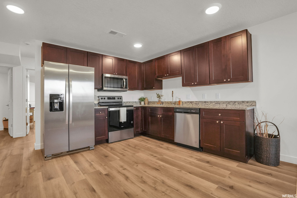 Kitchen with light stone countertops, appliances with stainless steel finishes, and light hardwood / wood-style floors