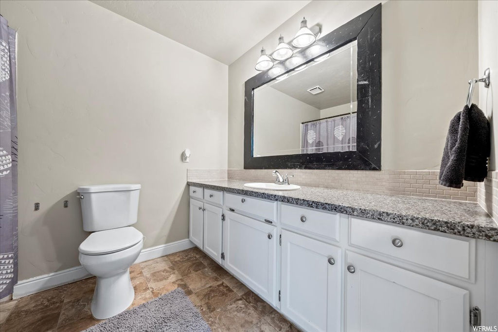 Bathroom featuring vanity, toilet, tile flooring, and backsplash