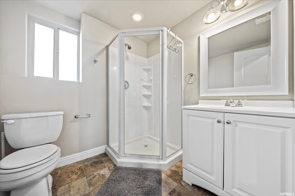 Bathroom featuring toilet, a shower with door, vanity with extensive cabinet space, and tile flooring