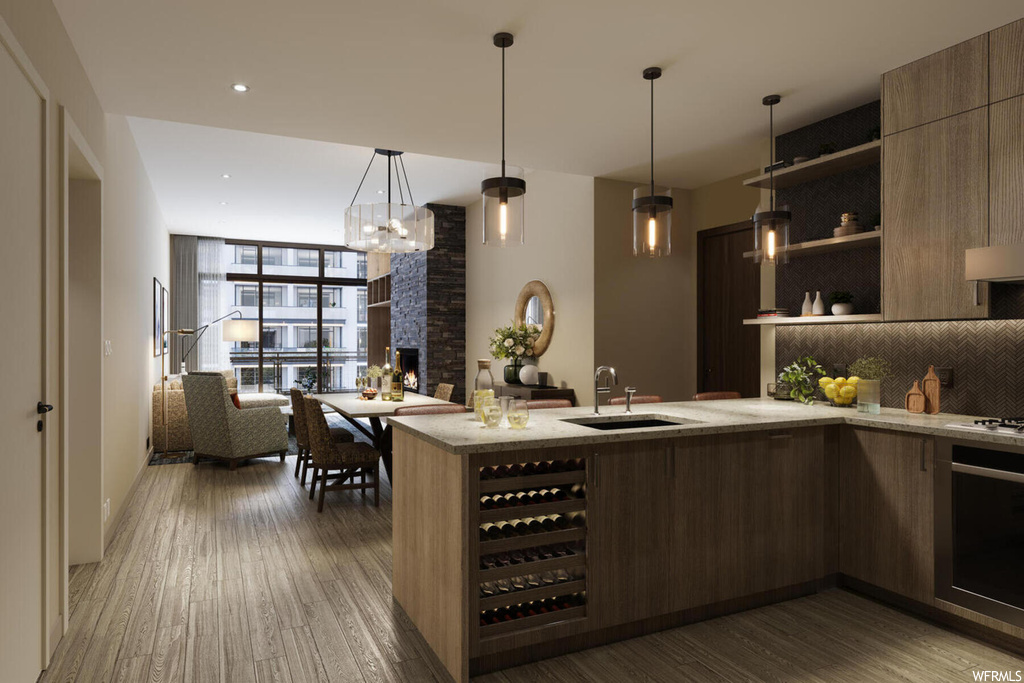 Kitchen featuring beverage cooler, hardwood / wood-style floors, sink, pendant lighting, and a stone fireplace