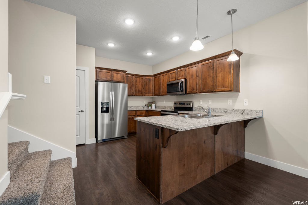 Kitchen with dark hardwood / wood-style floors, sink, decorative light fixtures, and appliances with stainless steel finishes