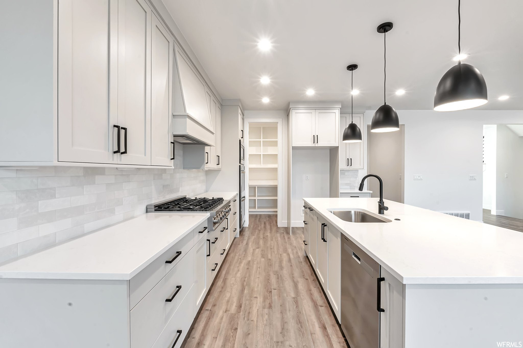Kitchen with sink, light hardwood / wood-style flooring, stainless steel dishwasher, pendant lighting, and an island with sink