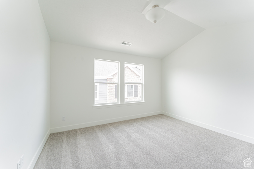 Empty room with light carpet and lofted ceiling