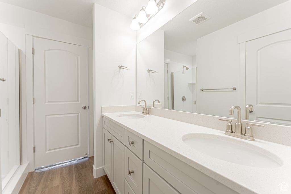 Bathroom featuring hardwood / wood-style floors, a shower with door, dual sinks, and vanity with extensive cabinet space