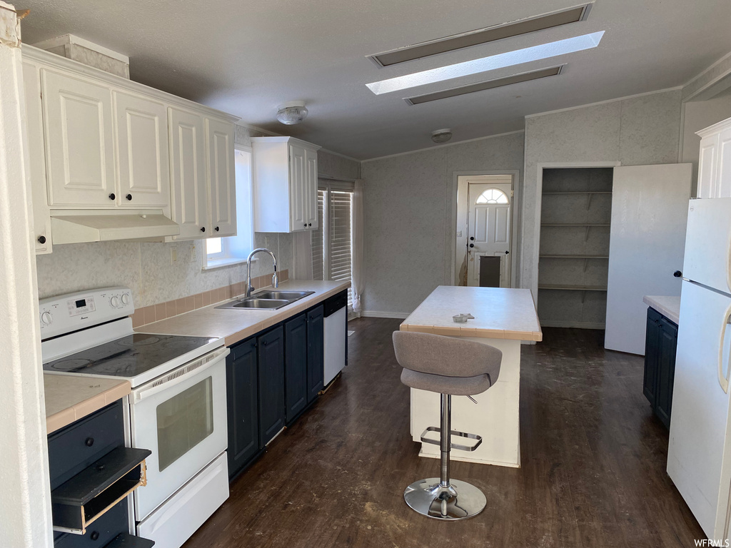 Kitchen with dark hardwood / wood-style flooring, sink, white appliances, a breakfast bar area, and white cabinetry