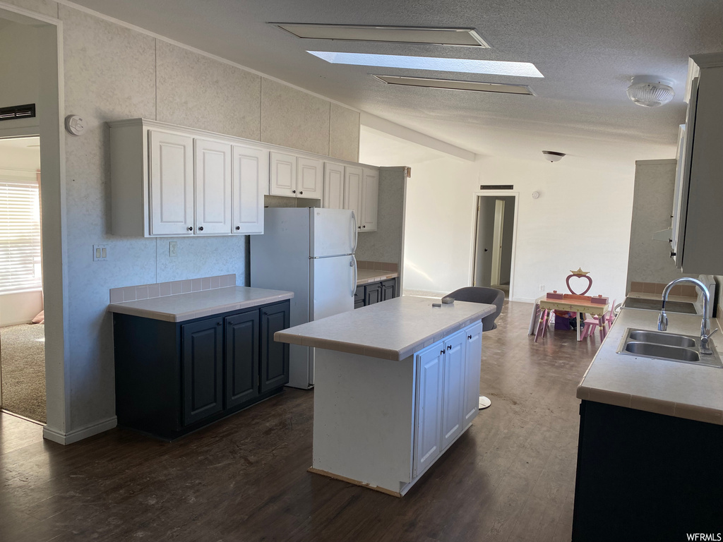 Kitchen featuring sink, vaulted ceiling with skylight, dark hardwood / wood-style floors, white fridge, and white cabinetry