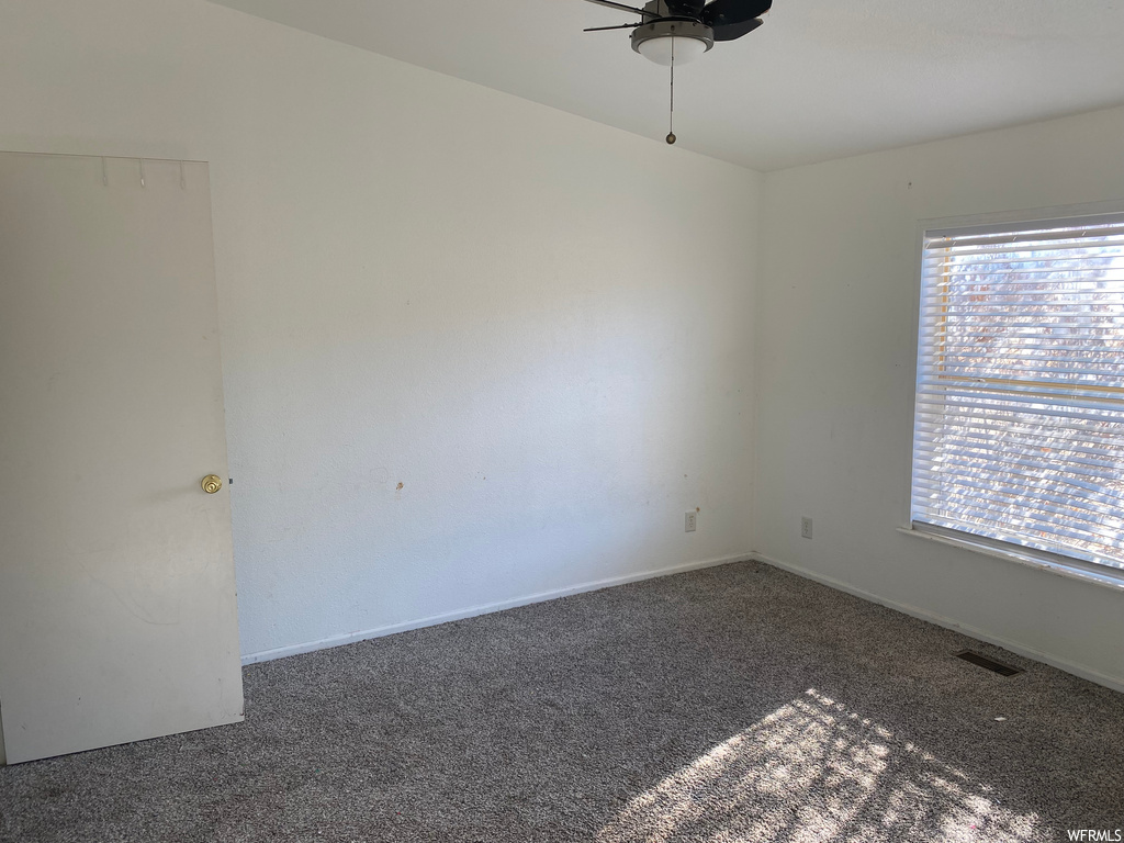 Unfurnished room featuring dark colored carpet, ceiling fan, and a healthy amount of sunlight