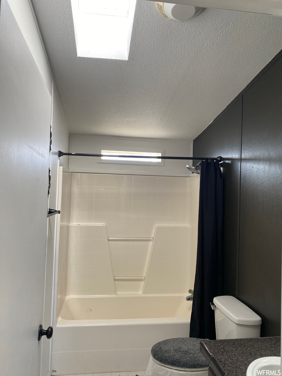 Full bathroom with a textured ceiling, vanity, toilet, and shower / tub combo