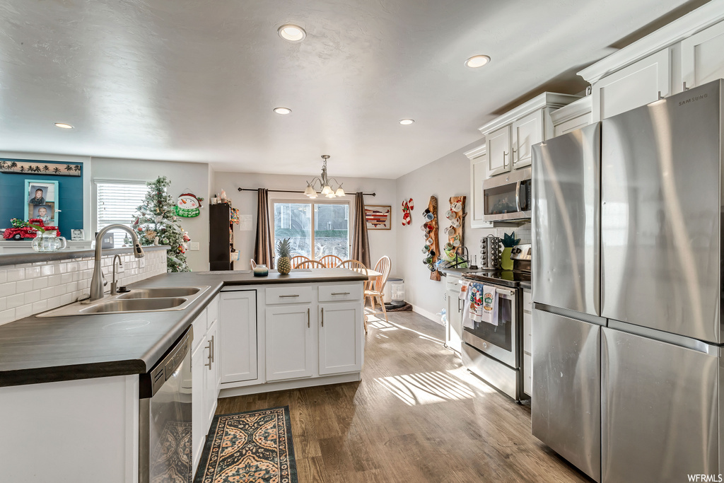 Kitchen with white cabinetry, stainless steel appliances, a notable chandelier, decorative light fixtures, and hardwood / wood-style floors