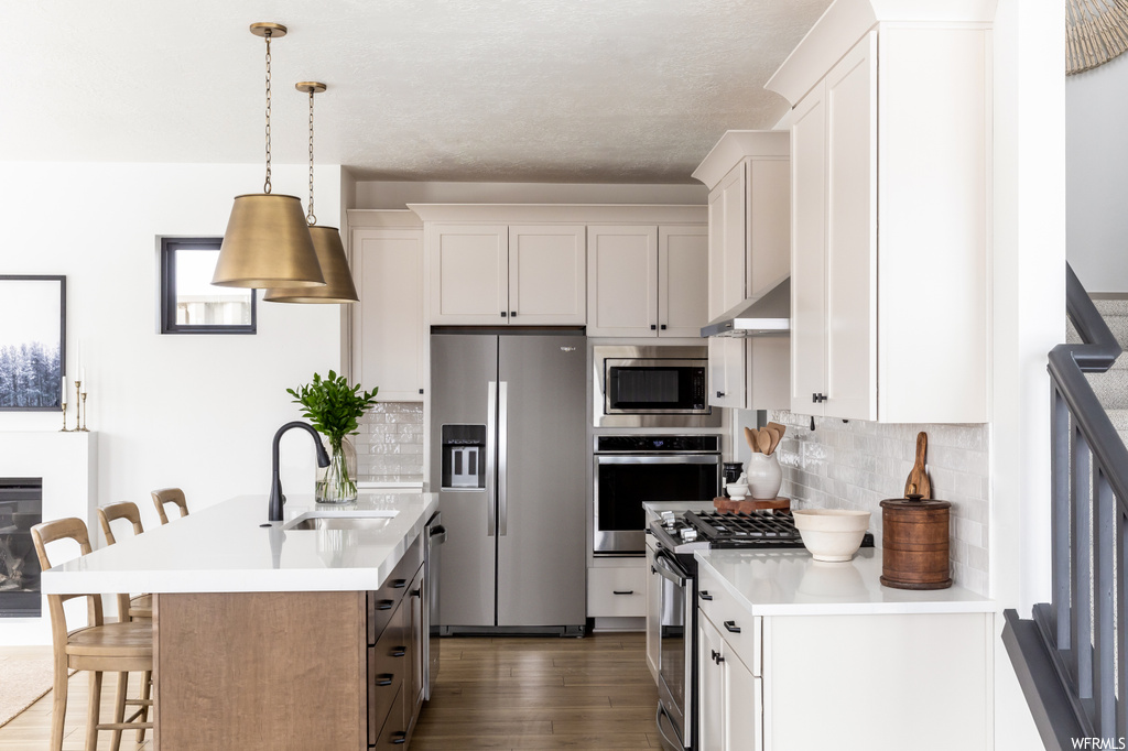 Kitchen featuring a breakfast bar area, hanging light fixtures, appliances with stainless steel finishes, dark hardwood / wood-style floors, and tasteful backsplash