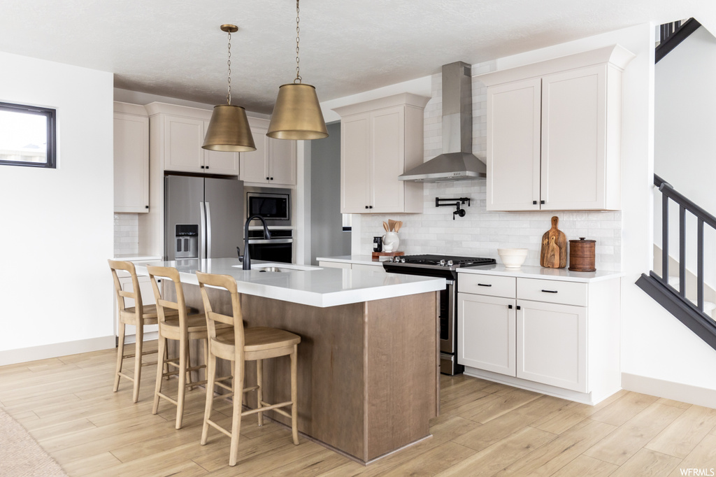 Kitchen with backsplash, hanging light fixtures, appliances with stainless steel finishes, wall chimney exhaust hood, and white cabinetry