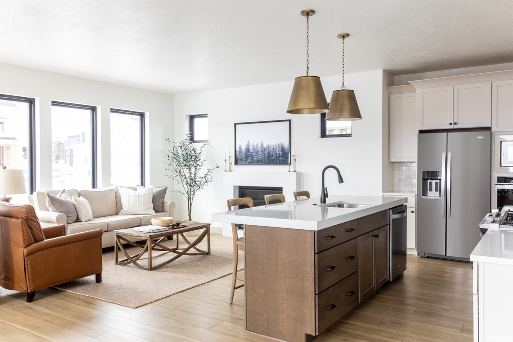 Kitchen with sink, a kitchen island with sink, light hardwood / wood-style floors, stainless steel appliances, and white cabinetry