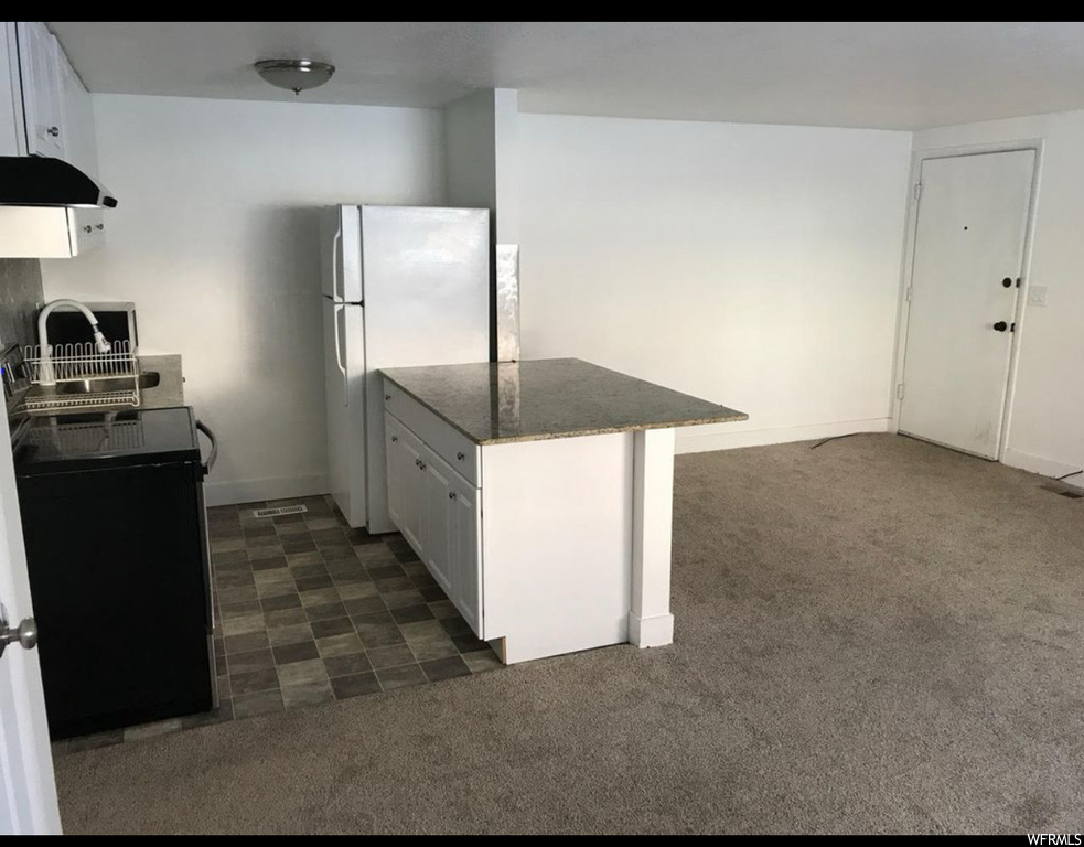 Kitchen with white fridge, dark stone countertops, stove, white cabinets, and dark carpet
