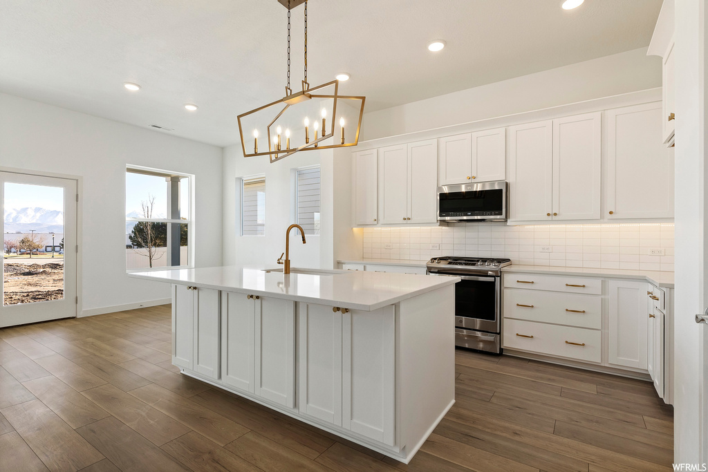 Kitchen featuring a center island with sink, appliances with stainless steel finishes, backsplash, and white cabinetry
