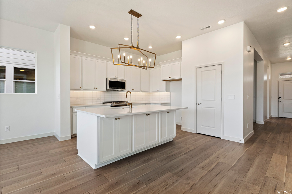 Kitchen with a kitchen island with sink, tasteful backsplash, white cabinets, and hardwood / wood-style flooring