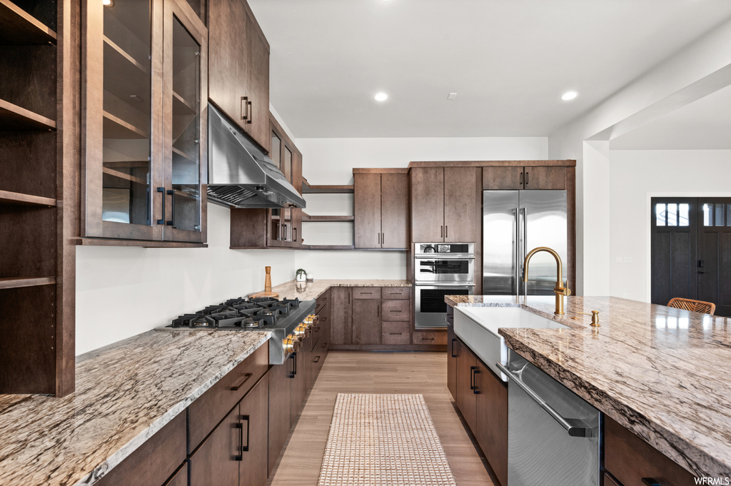 Kitchen featuring sink, light hardwood / wood-style floors, appliances with stainless steel finishes, dark brown cabinetry, and light stone counters