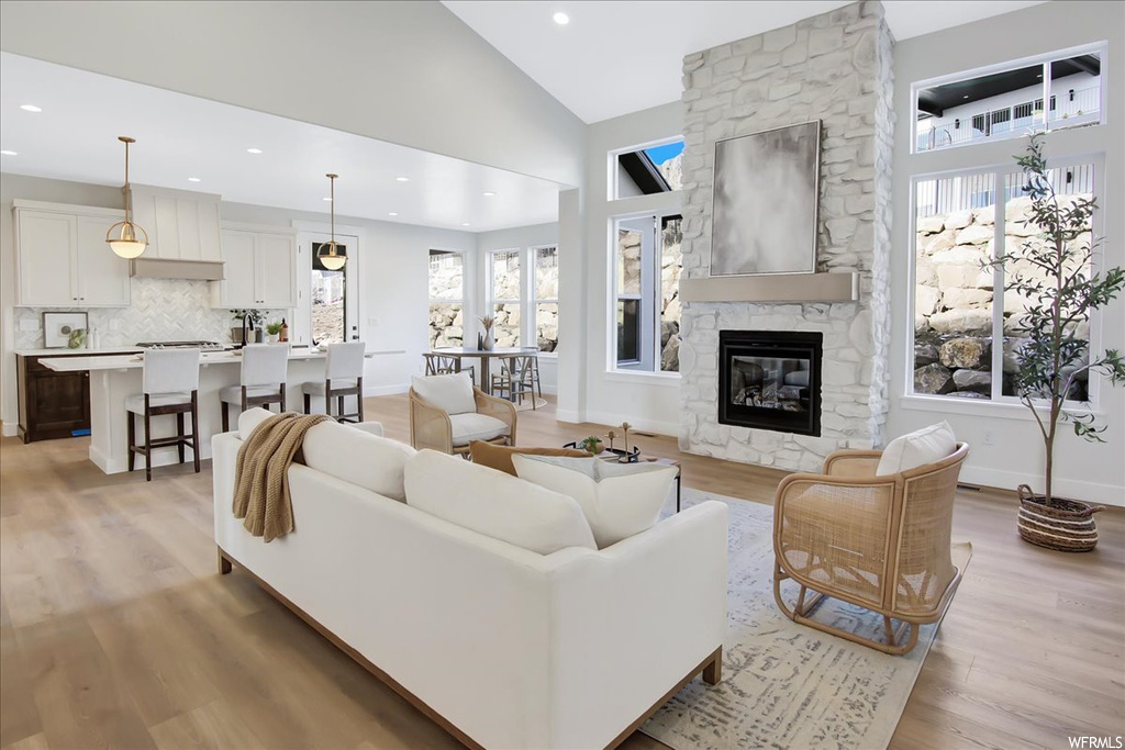 Living room featuring light hardwood / wood-style flooring, a stone fireplace, and high vaulted ceiling