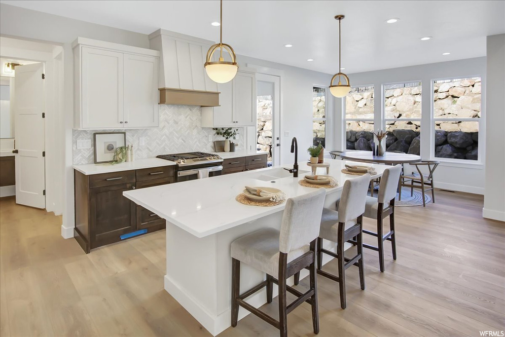 Kitchen featuring a center island with sink, gas stove, and white cabinetry