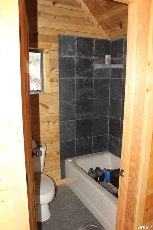 Bathroom featuring toilet, shower / washtub combination, wooden ceiling, wooden walls, and tile floors