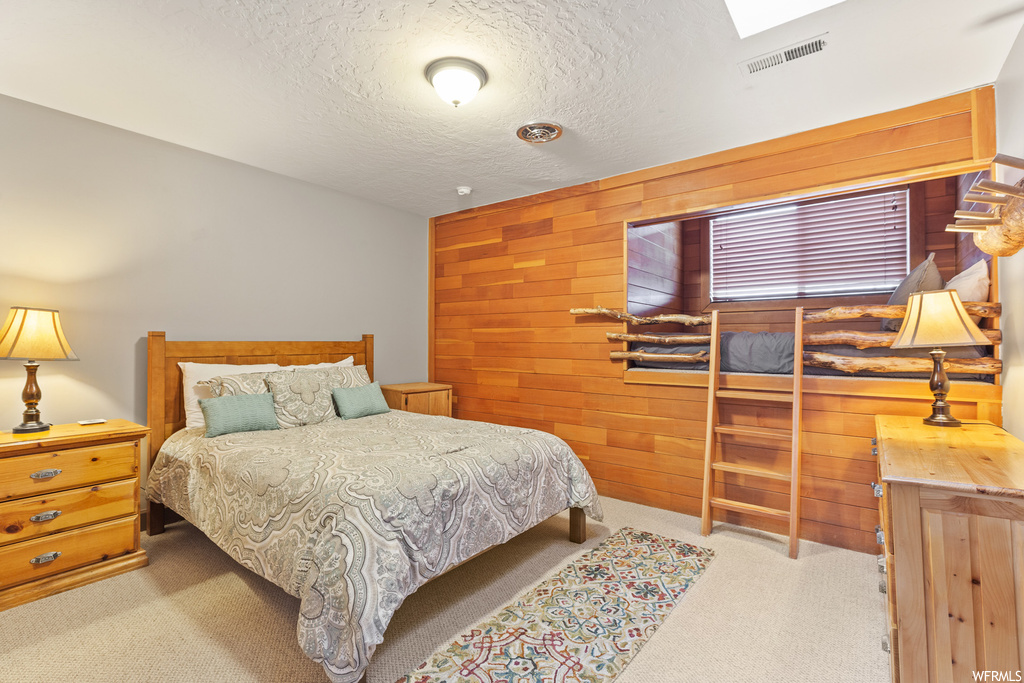 Bedroom with a textured ceiling, light colored carpet, and wooden walls
