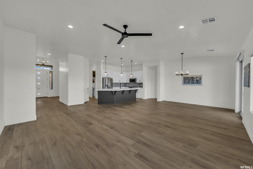 Unfurnished living room featuring dark wood-type flooring and ceiling fan with notable chandelier