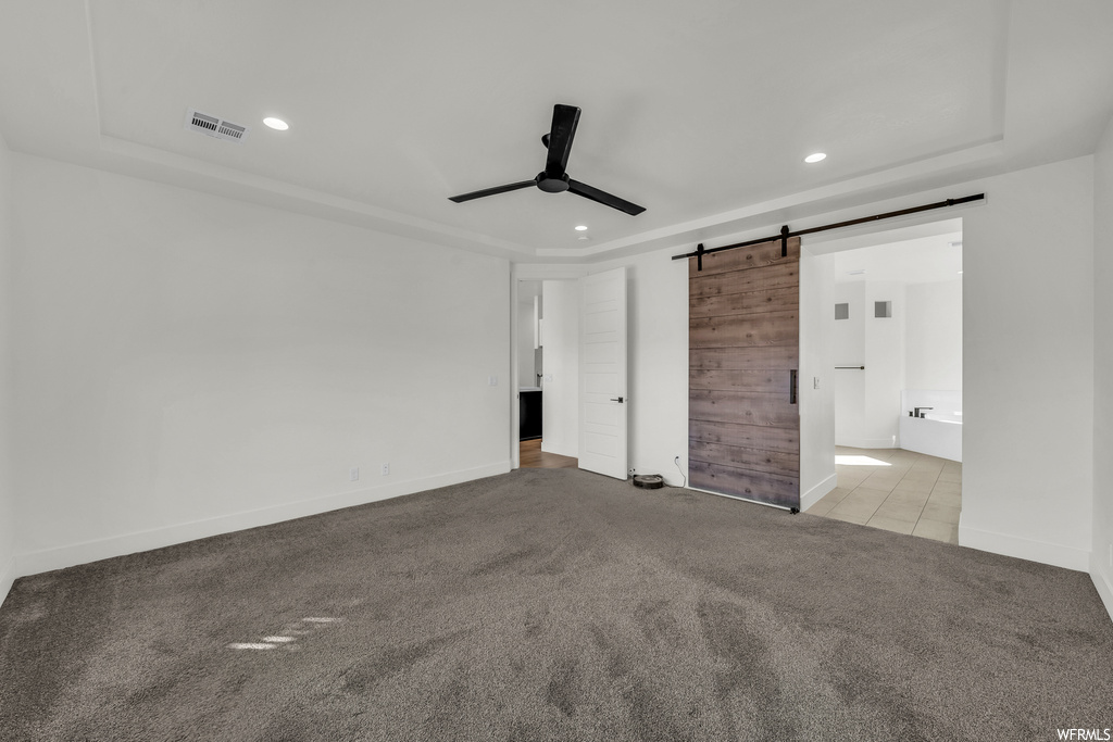 Unfurnished bedroom with connected bathroom, ceiling fan, a barn door, and light colored carpet