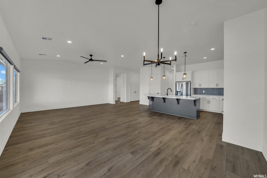 Unfurnished living room with dark hardwood / wood-style floors, sink, and ceiling fan with notable chandelier