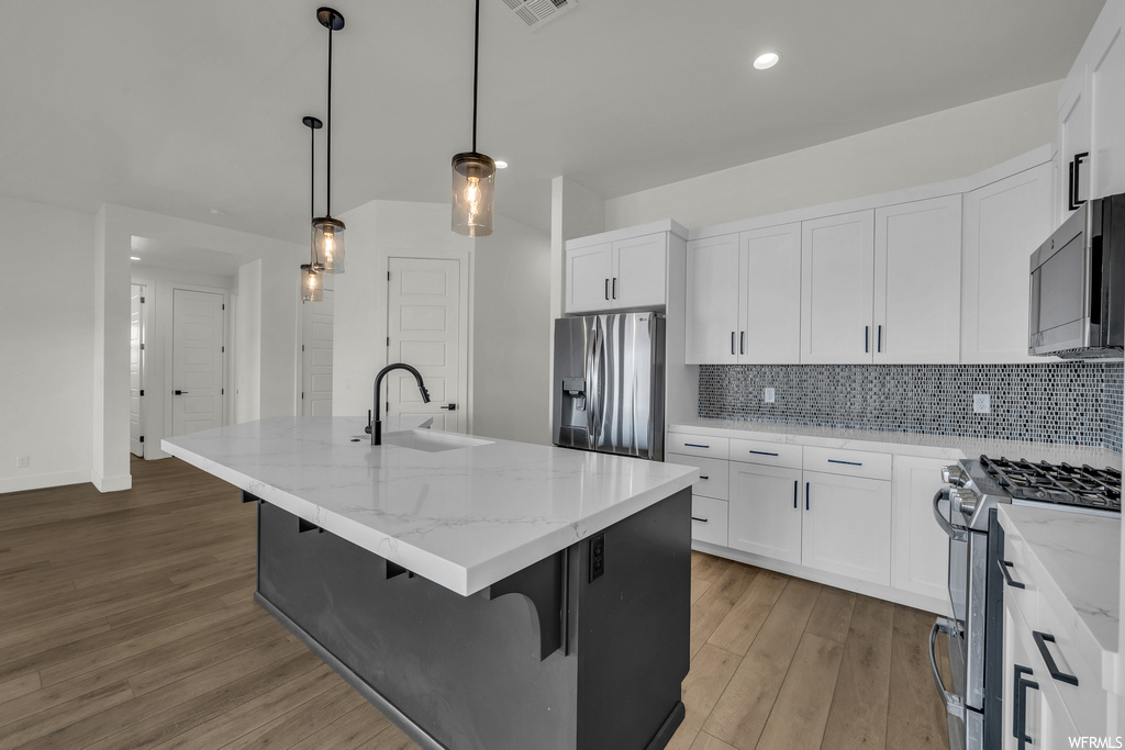 Kitchen with sink, appliances with stainless steel finishes, white cabinetry, and wood-type flooring