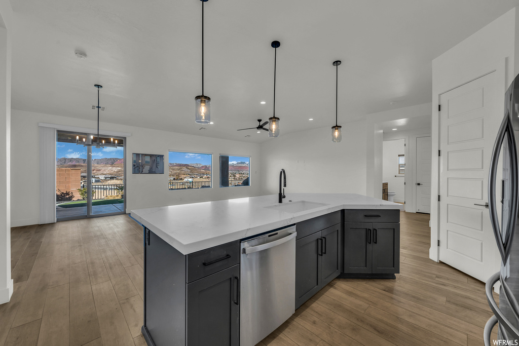 Kitchen featuring sink, light hardwood / wood-style flooring, ceiling fan with notable chandelier, stainless steel dishwasher, and pendant lighting