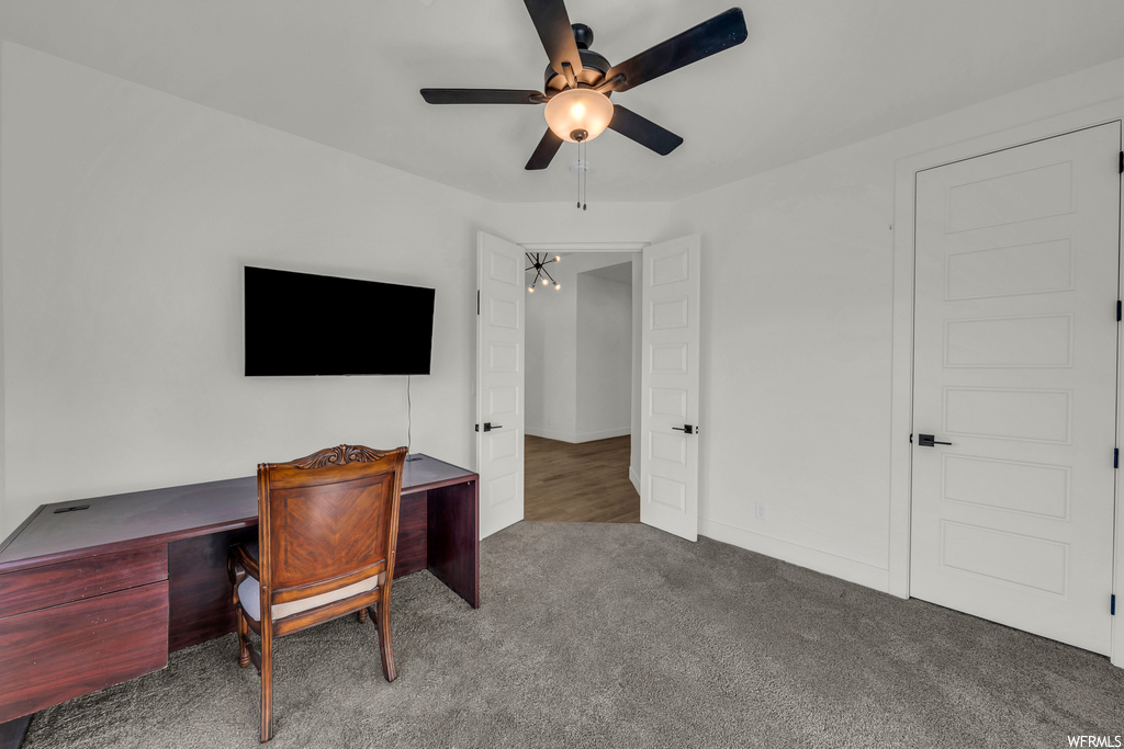 Office space featuring dark colored carpet and ceiling fan with notable chandelier