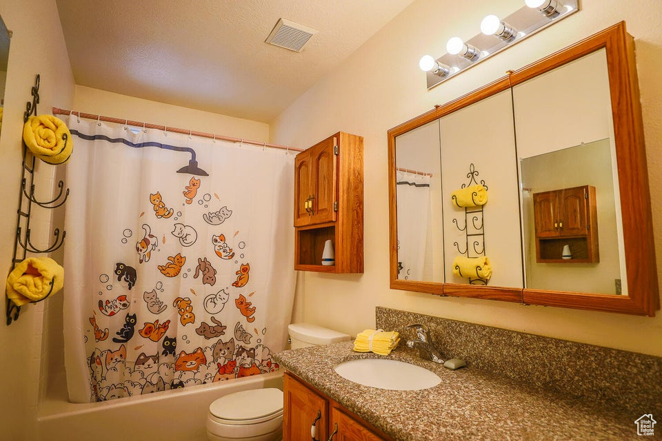 Full bathroom featuring shower / bathtub combination with curtain, toilet, vanity, and a textured ceiling