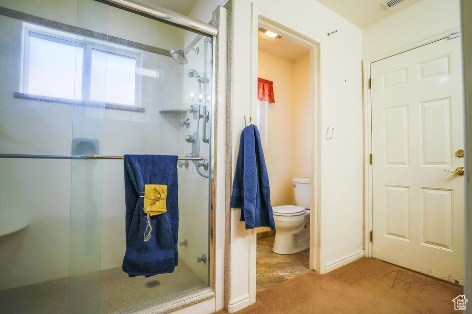 Bathroom featuring a shower with door, toilet, and tile flooring