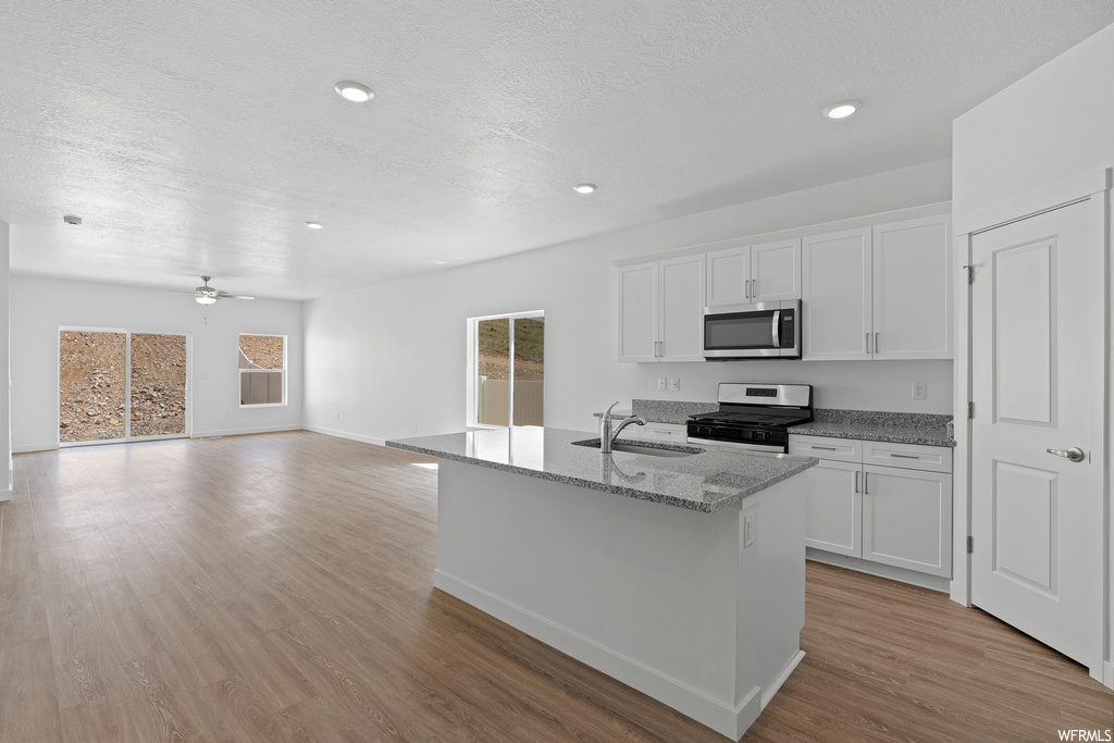 Kitchen with stainless steel appliances, light wood-type flooring, ceiling fan, white cabinets, and an island with sink
