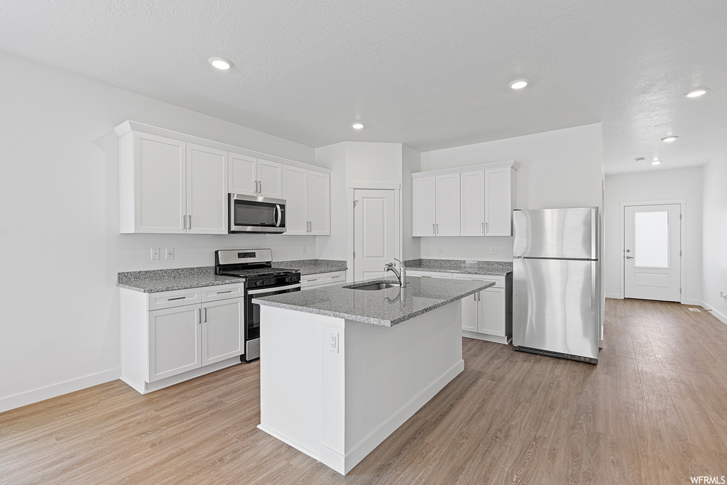 Kitchen featuring sink, light hardwood / wood-style floors, appliances with stainless steel finishes, white cabinets, and a center island with sink