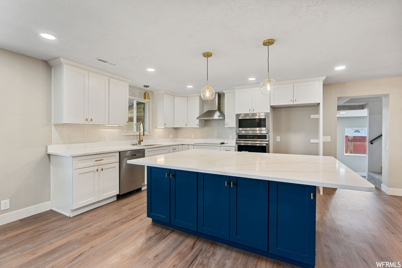 Kitchen featuring a center island, light hardwood / wood-style floors, stainless steel appliances, decorative light fixtures, and backsplash
