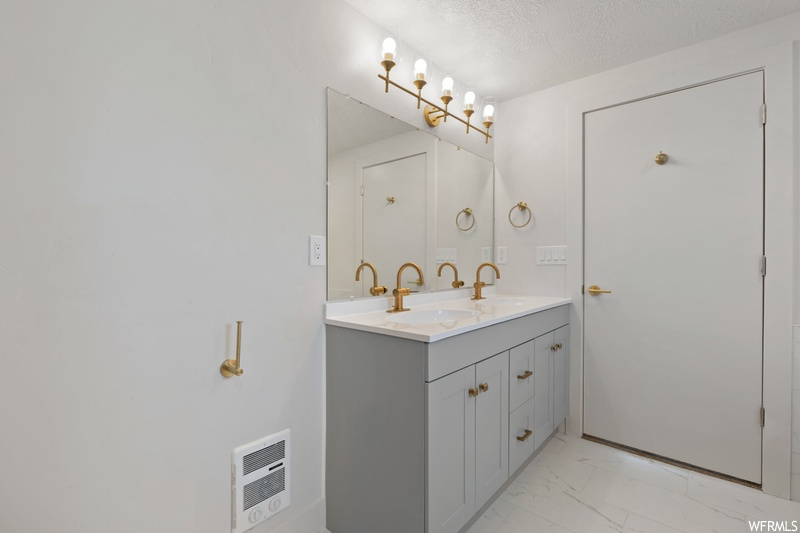 Bathroom featuring dual sinks, an inviting chandelier, large vanity, a textured ceiling, and tile floors