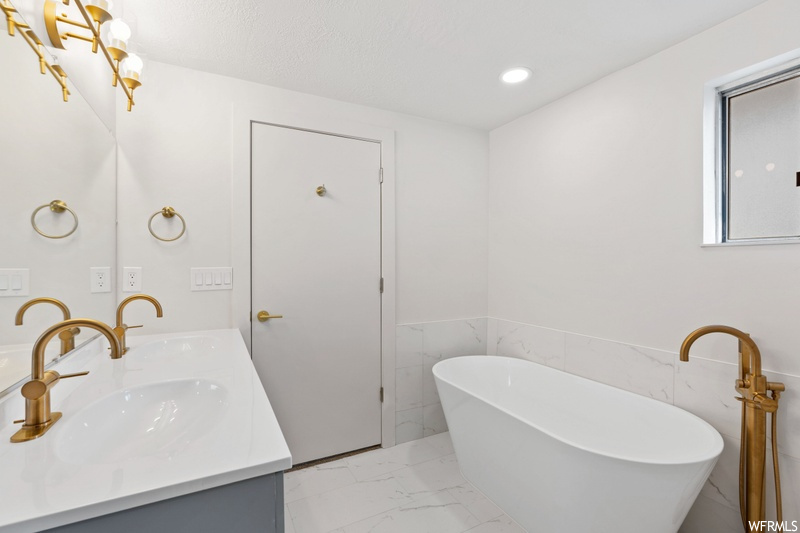 Bathroom with tile flooring, tile walls, a bathtub, and double sink vanity