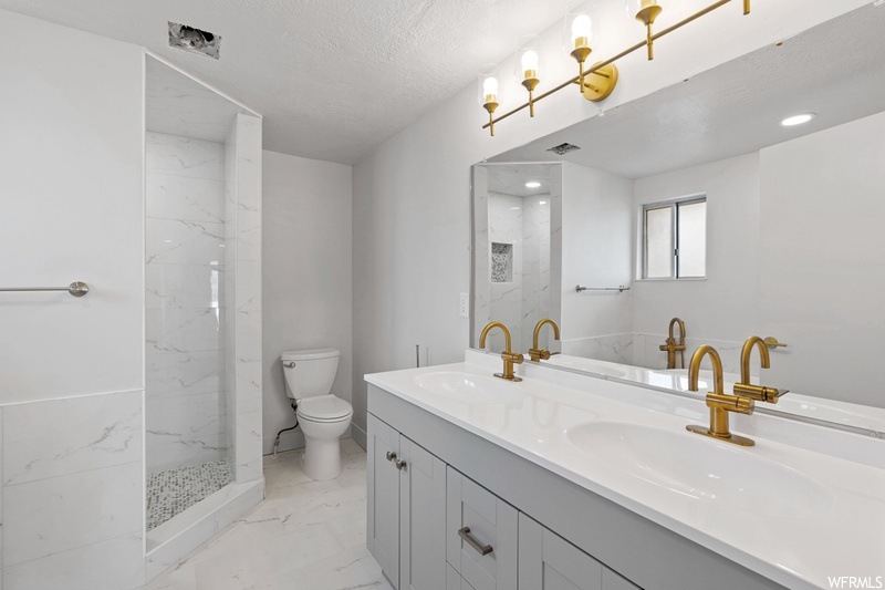 Bathroom featuring dual sinks, toilet, a textured ceiling, oversized vanity, and tile floors