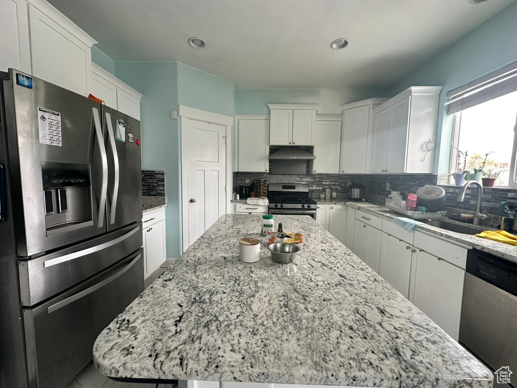 Kitchen with white cabinets, tasteful backsplash, appliances with stainless steel finishes, and a center island
