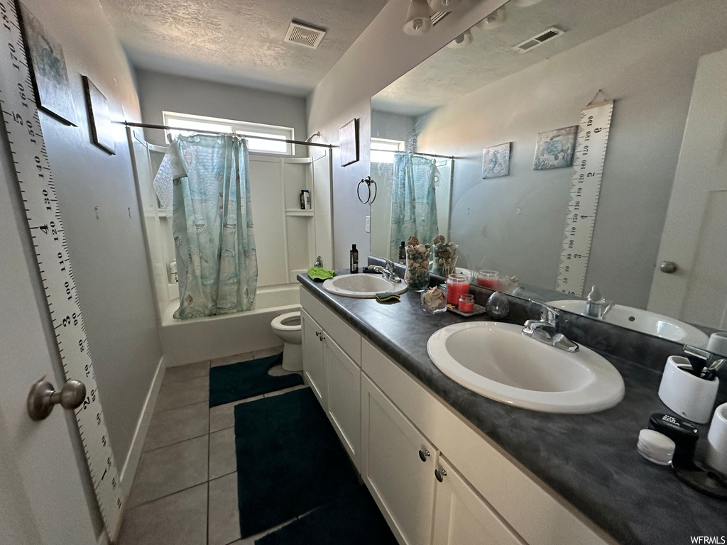 Full bathroom featuring toilet, a textured ceiling, tile flooring, dual bowl vanity, and shower / bath combo