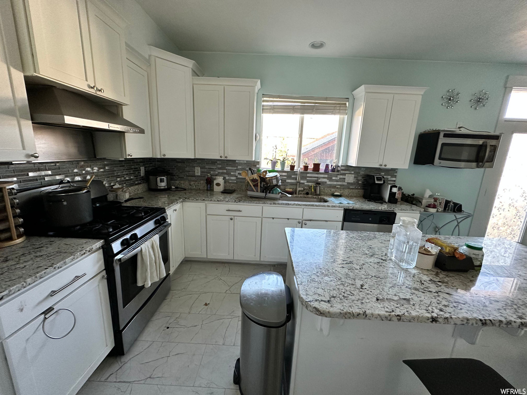 Kitchen with light tile floors, light stone countertops, stainless steel appliances, tasteful backsplash, and white cabinetry