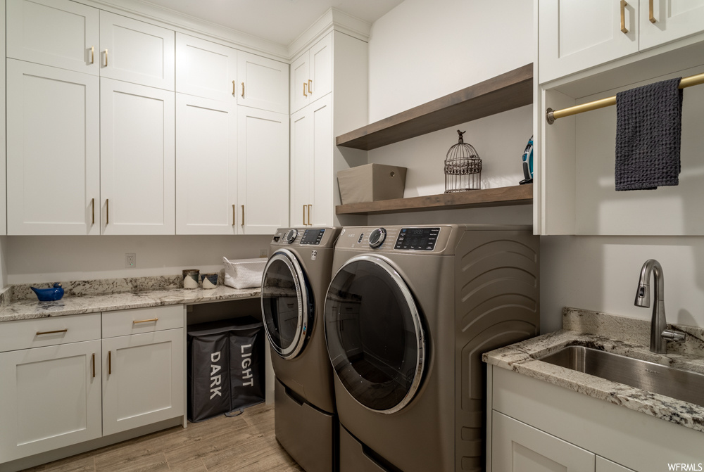 Laundry room with light wood-type flooring, cabinets, sink, and washing machine and dryer