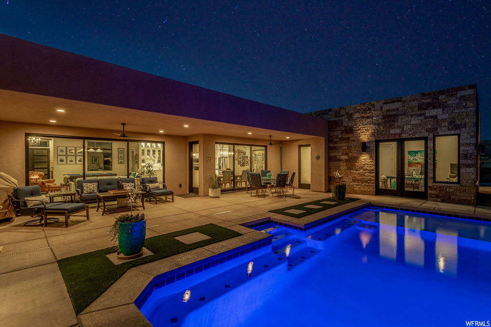 Pool at night featuring an outdoor living space, ceiling fan, a patio area, and a jacuzzi