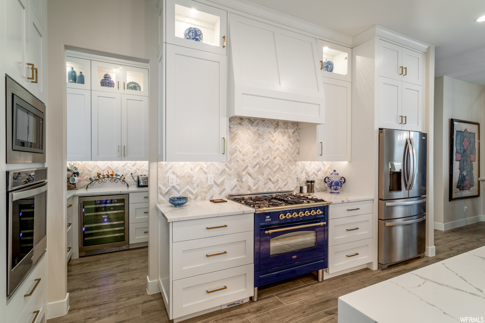 Kitchen featuring wine cooler, appliances with stainless steel finishes, backsplash, and white cabinetry