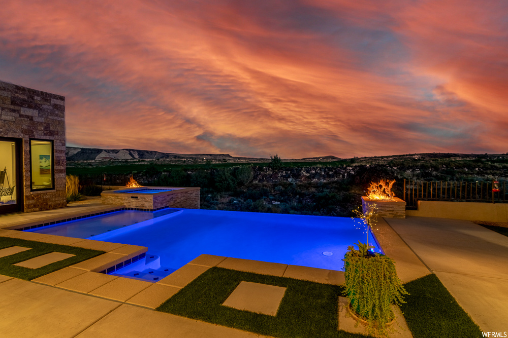 Pool at dusk with a patio area, an in ground hot tub, and a mountain view